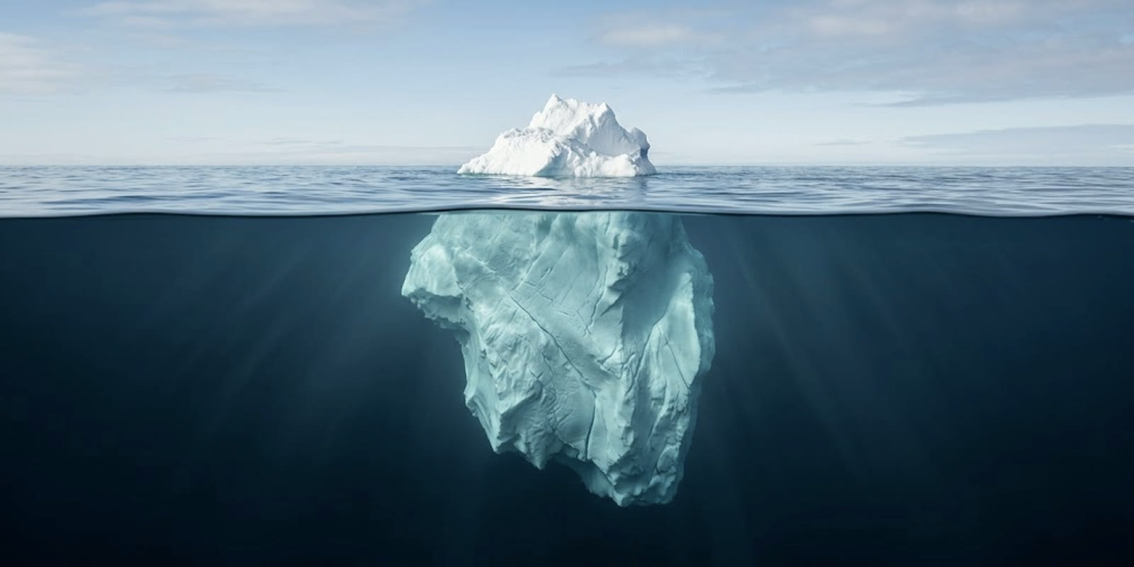 An iceberg split by the waterline, a small peak above the surface and a far larger mass below it