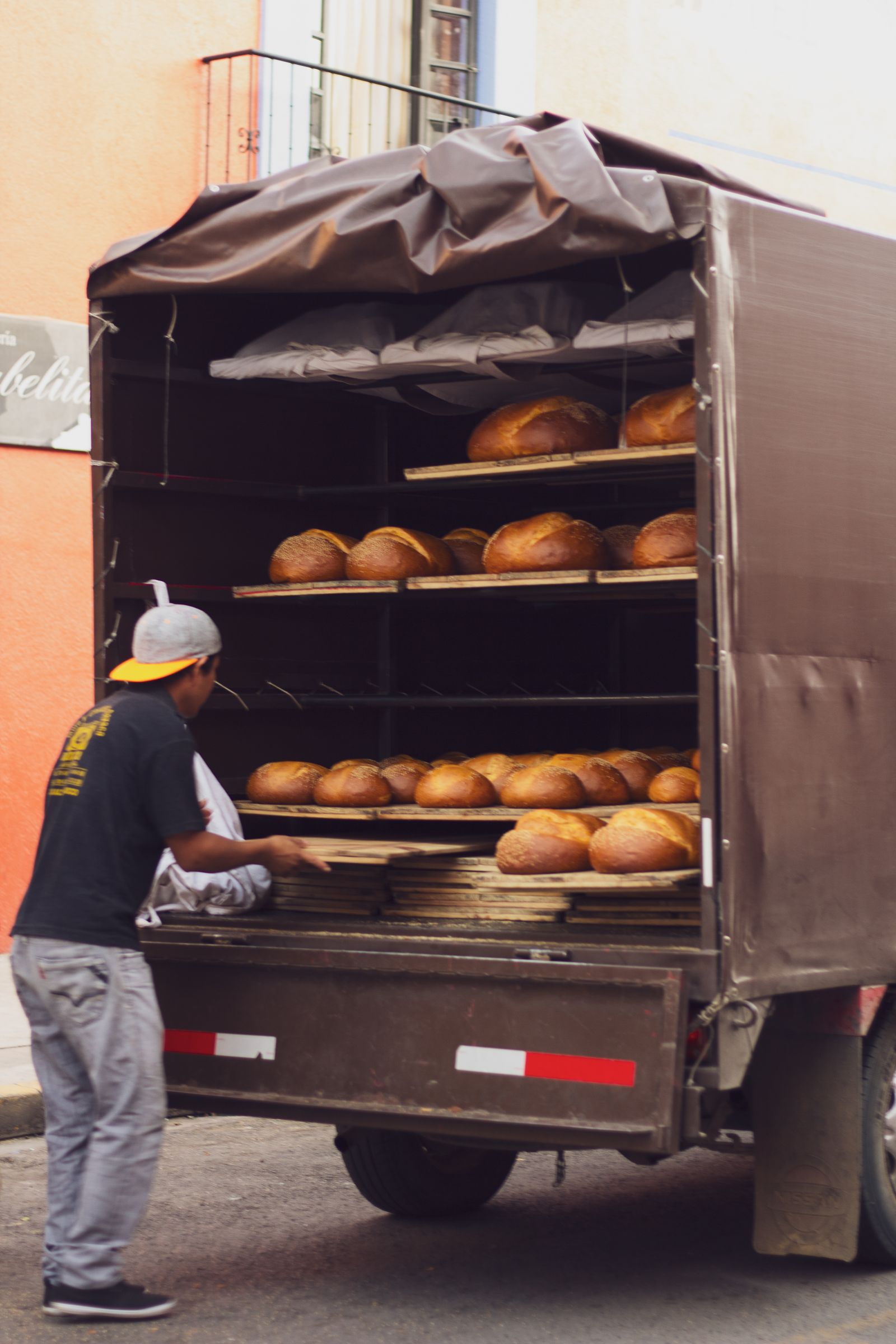 A worker loading trays of fresh bread into the back of a delivery truck